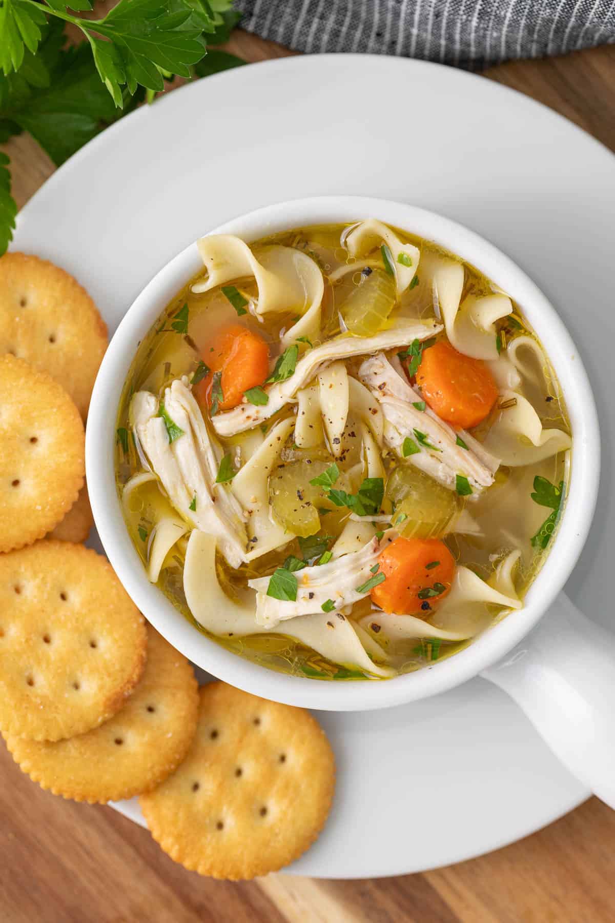 Chicken noodle soup in a white bowl on a plate with crackers.