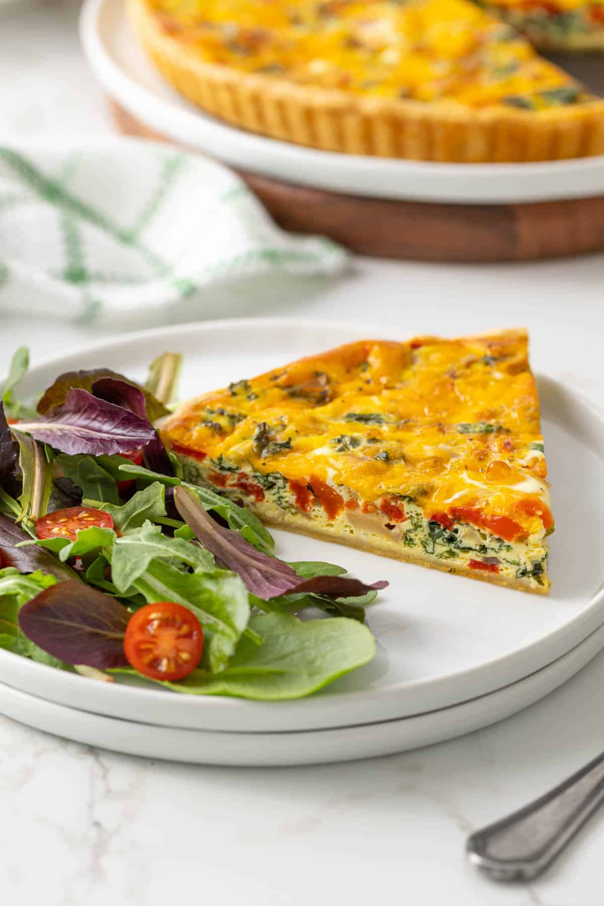 A slice of kale quiche on a white plate with a garden salad.