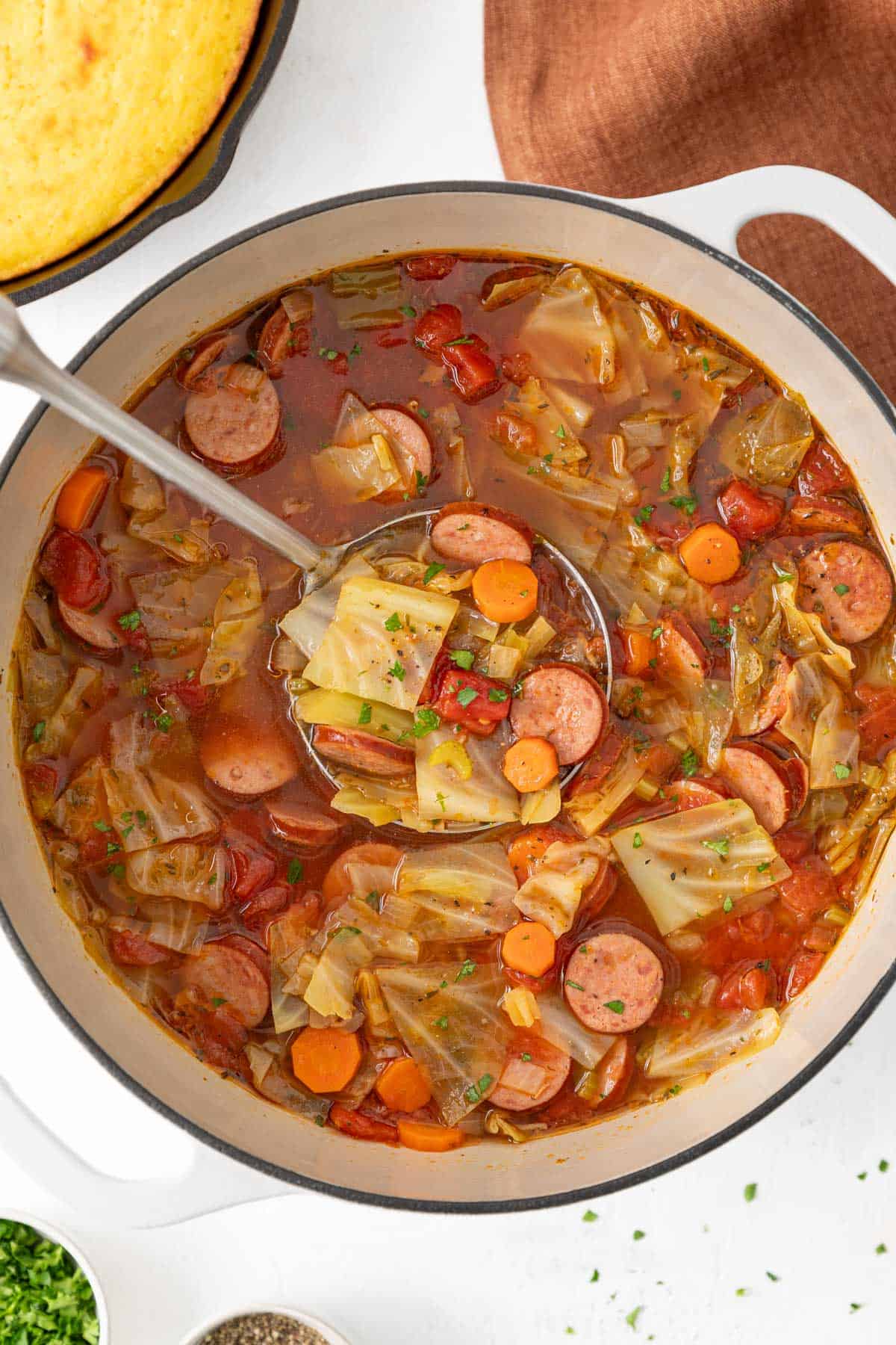 Overhead view of a ladle in a pot of sausage and cabbage soup.