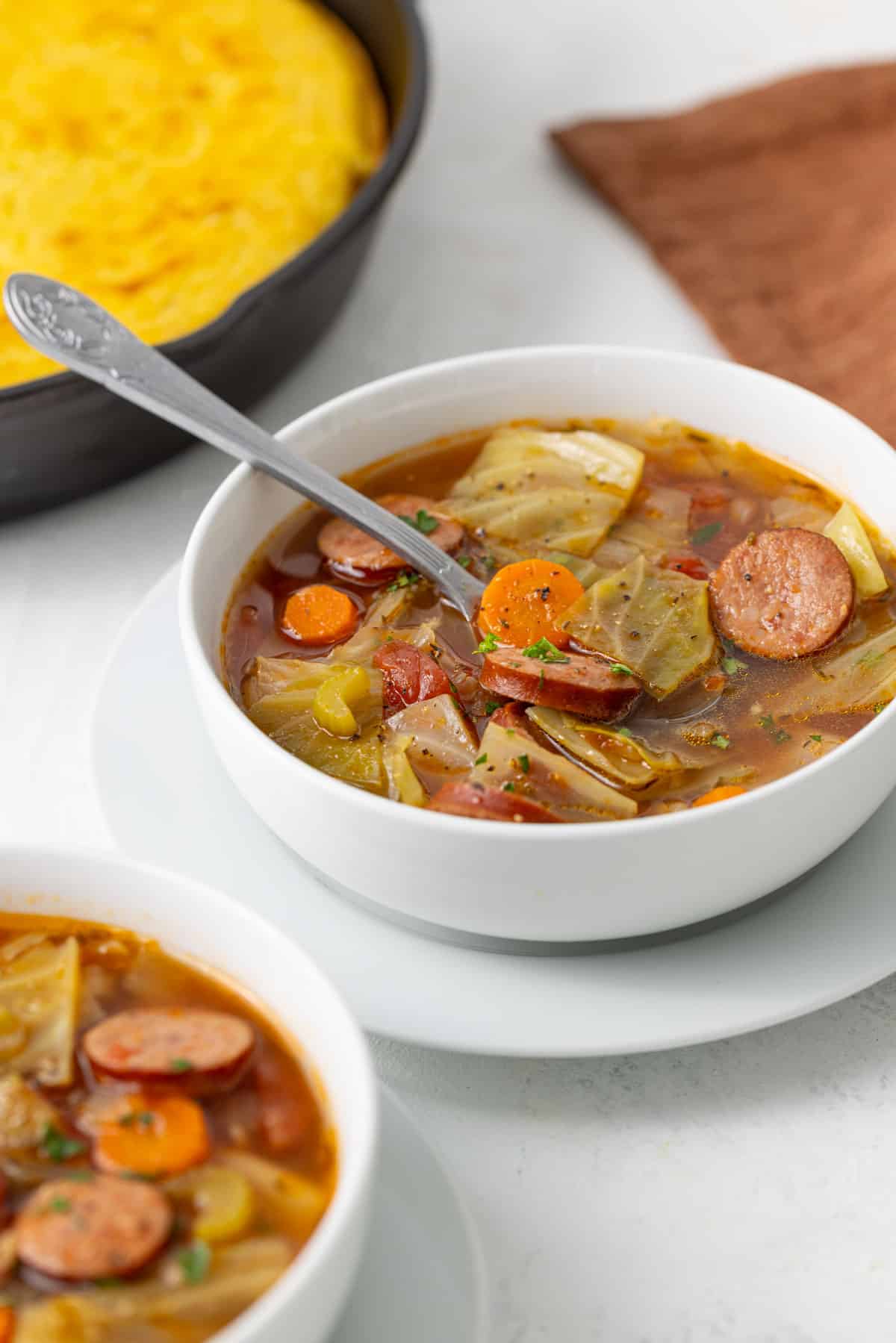 Front view of a spoon in a bowl of cabbage and sausage soup.