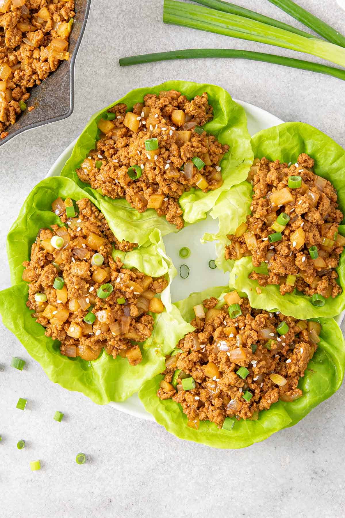 Overhead view of four ground turkey lettuce wraps on a white plate.