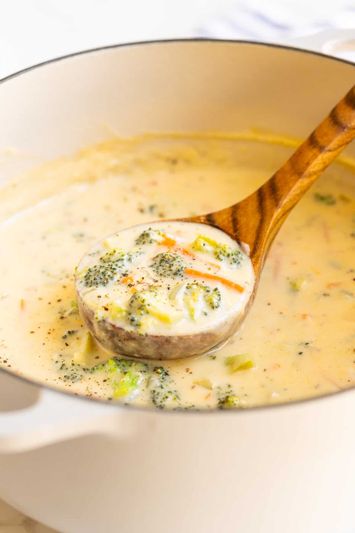 A wooden ladle in a pot of broccoli cheddar soup.