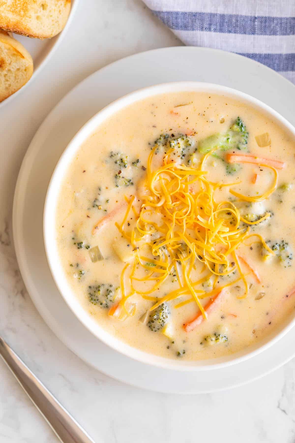 A bowl of broccoli cheddar soup sprinkled with shredded cheddar cheese.