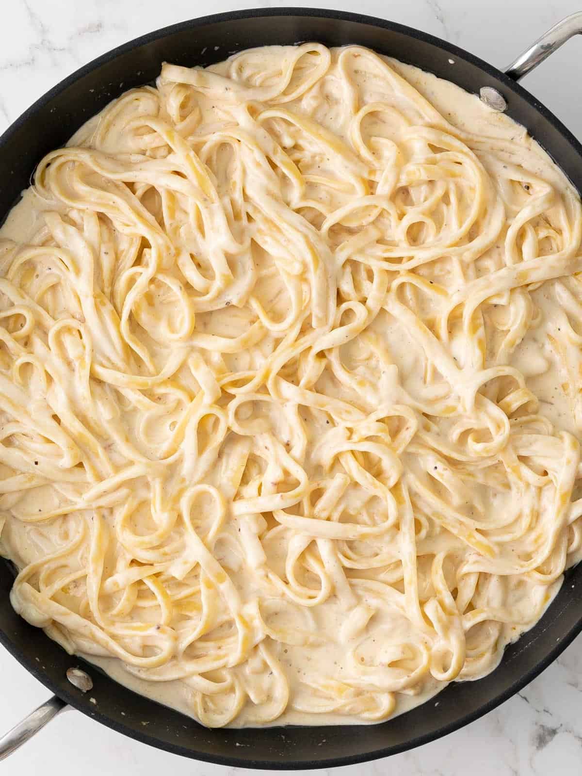 Fettuccine pasta tossed with alfredo sauce in a skillet.