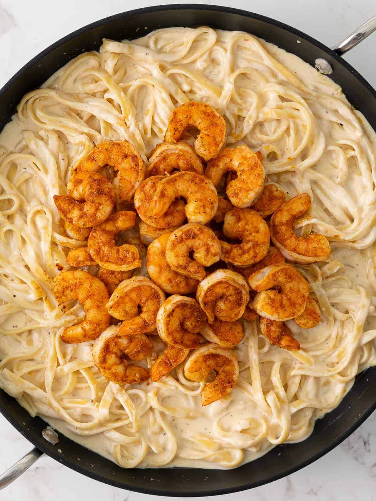 Fettuccini alfredo pasta topped with cajun shrimp in a skillet.