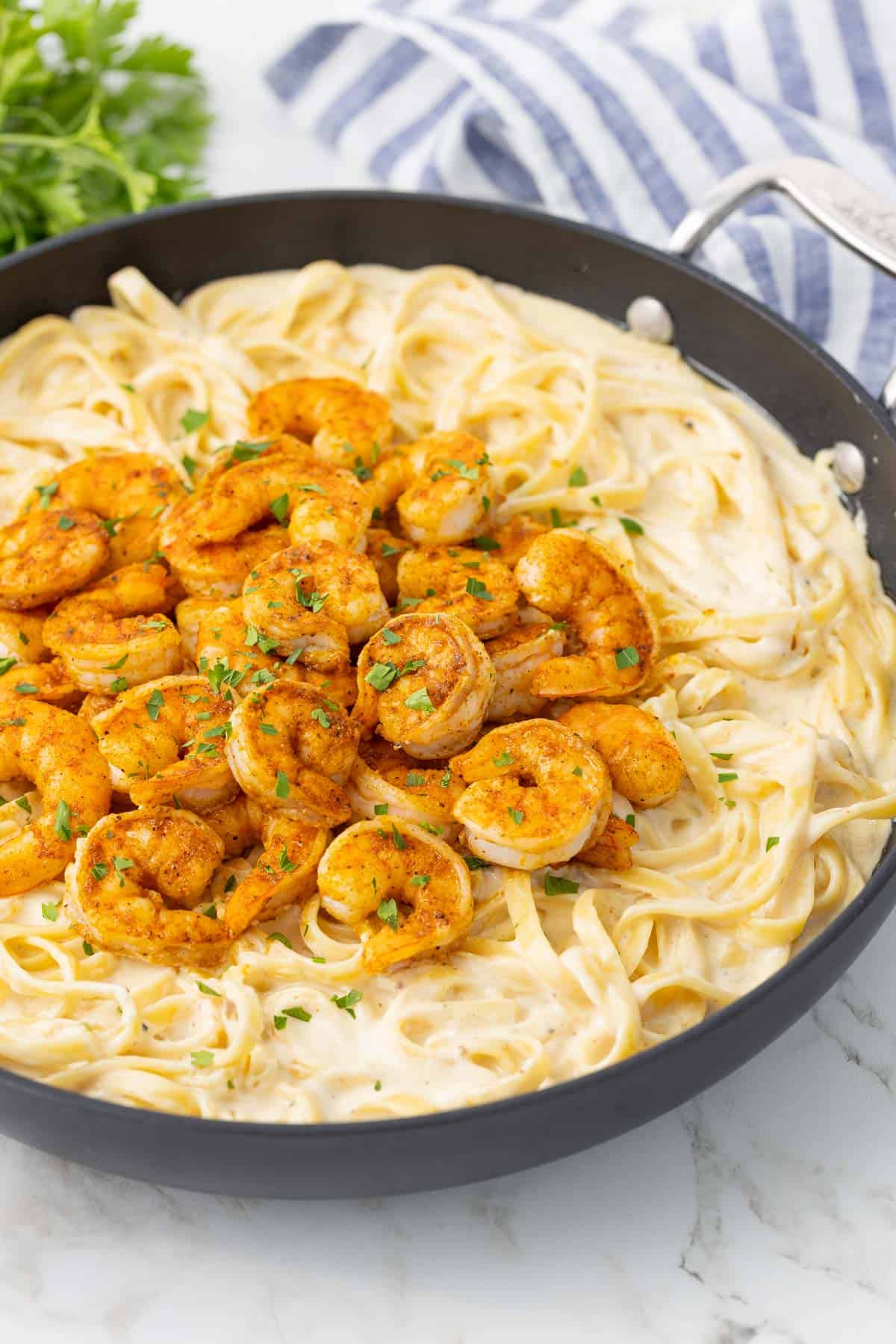 Cajun shrimp alfredo pasta in a skillet beside a blue and white striped kitchen towel.