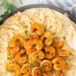 Cajun shrimp alfredo in a skillet. Overlay text is at the top of the image.