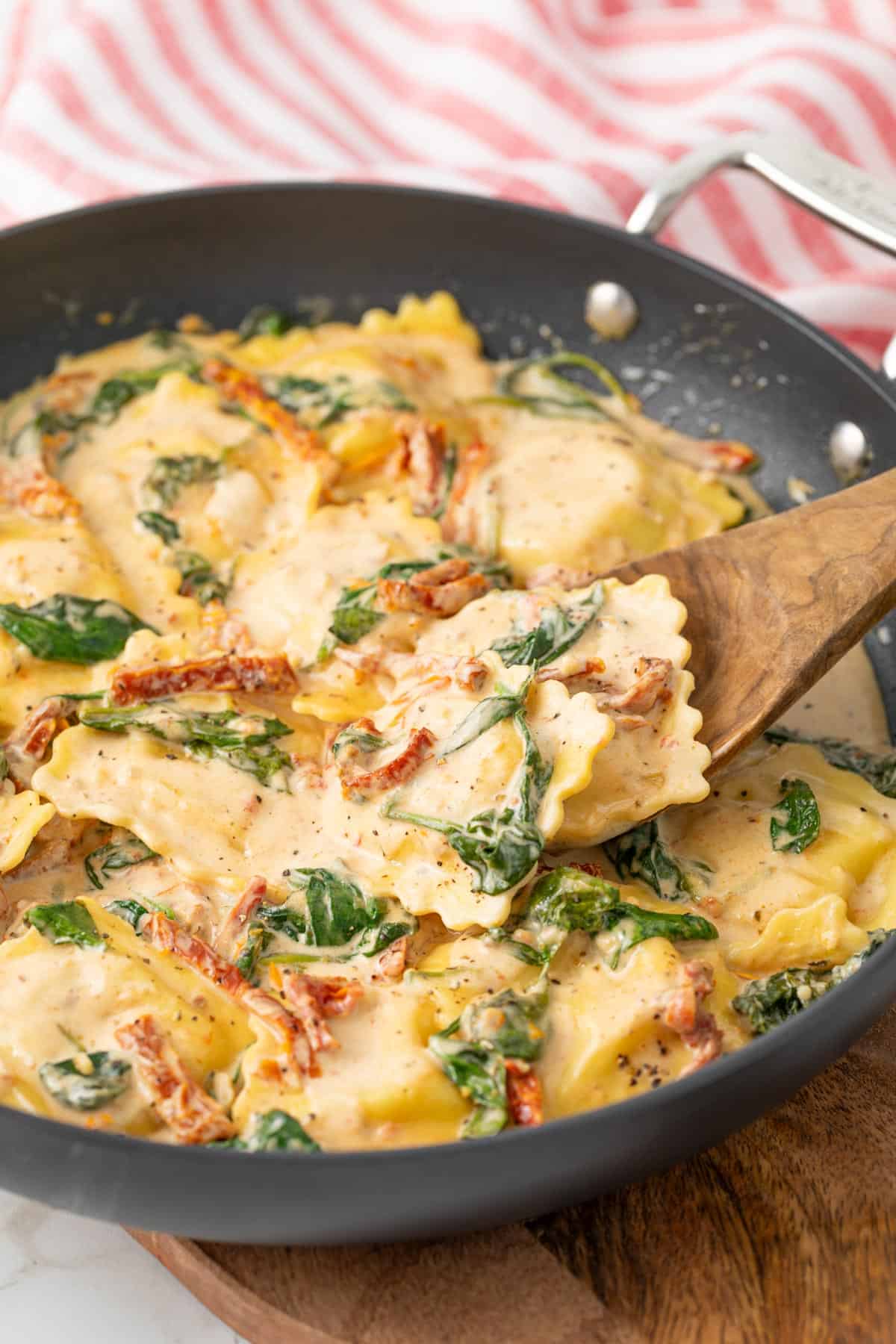 A wooden spoon in a skillet with creamy Tuscan ravioli.
