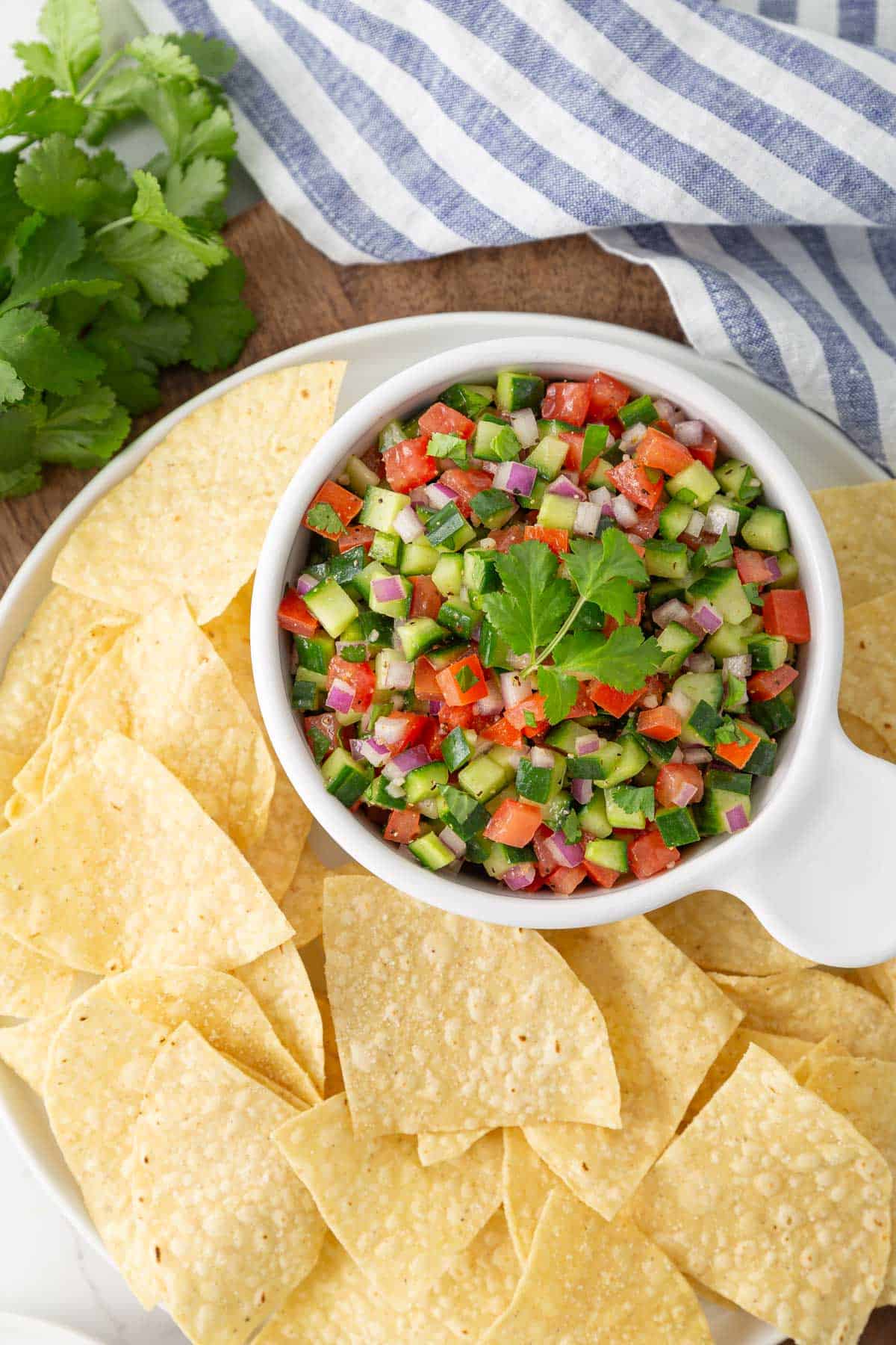 Cucumber salsa in a bowl on a platter with tortilla chips.