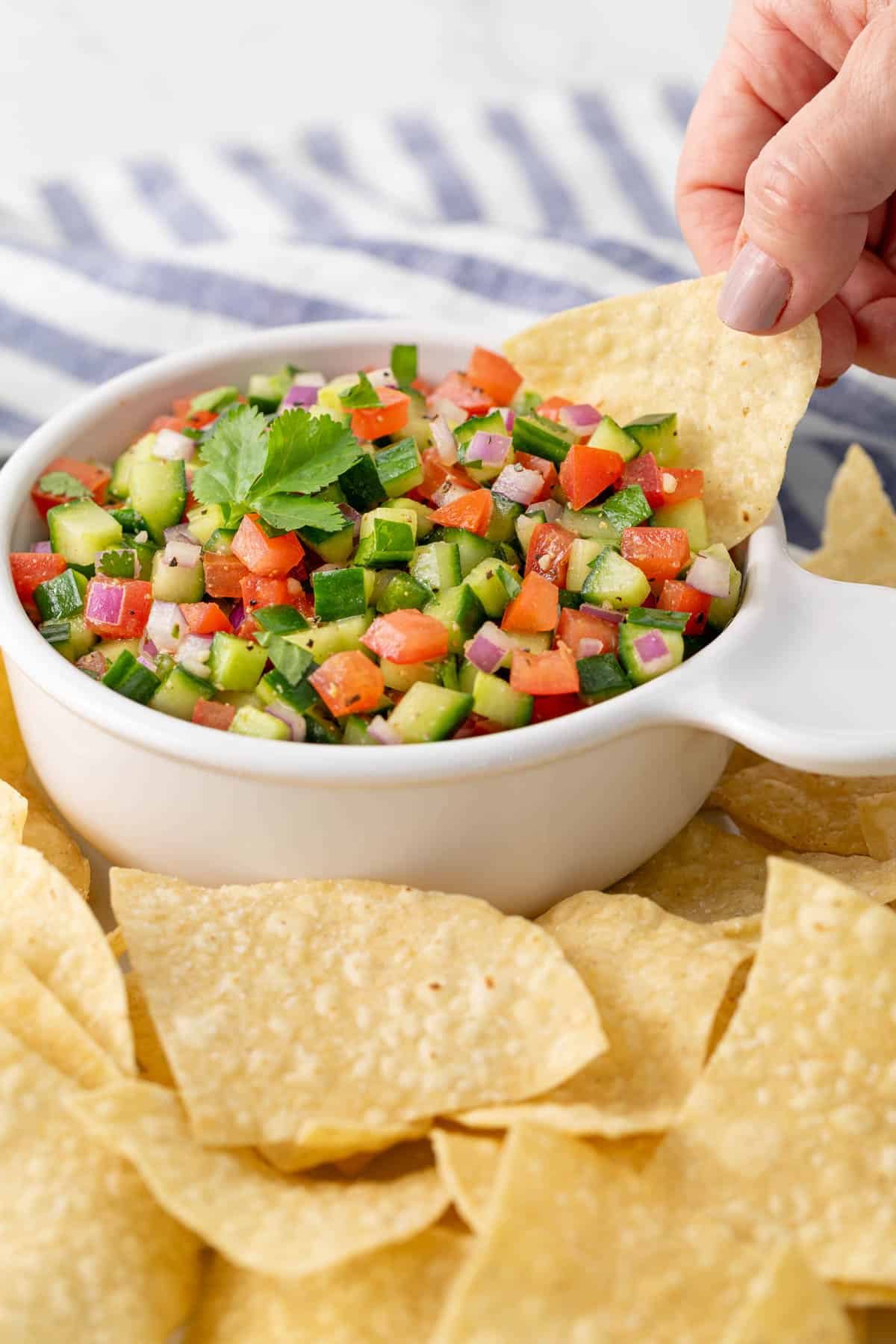 A tortilla chip is being dipped into a bowl of cucumber salsa.