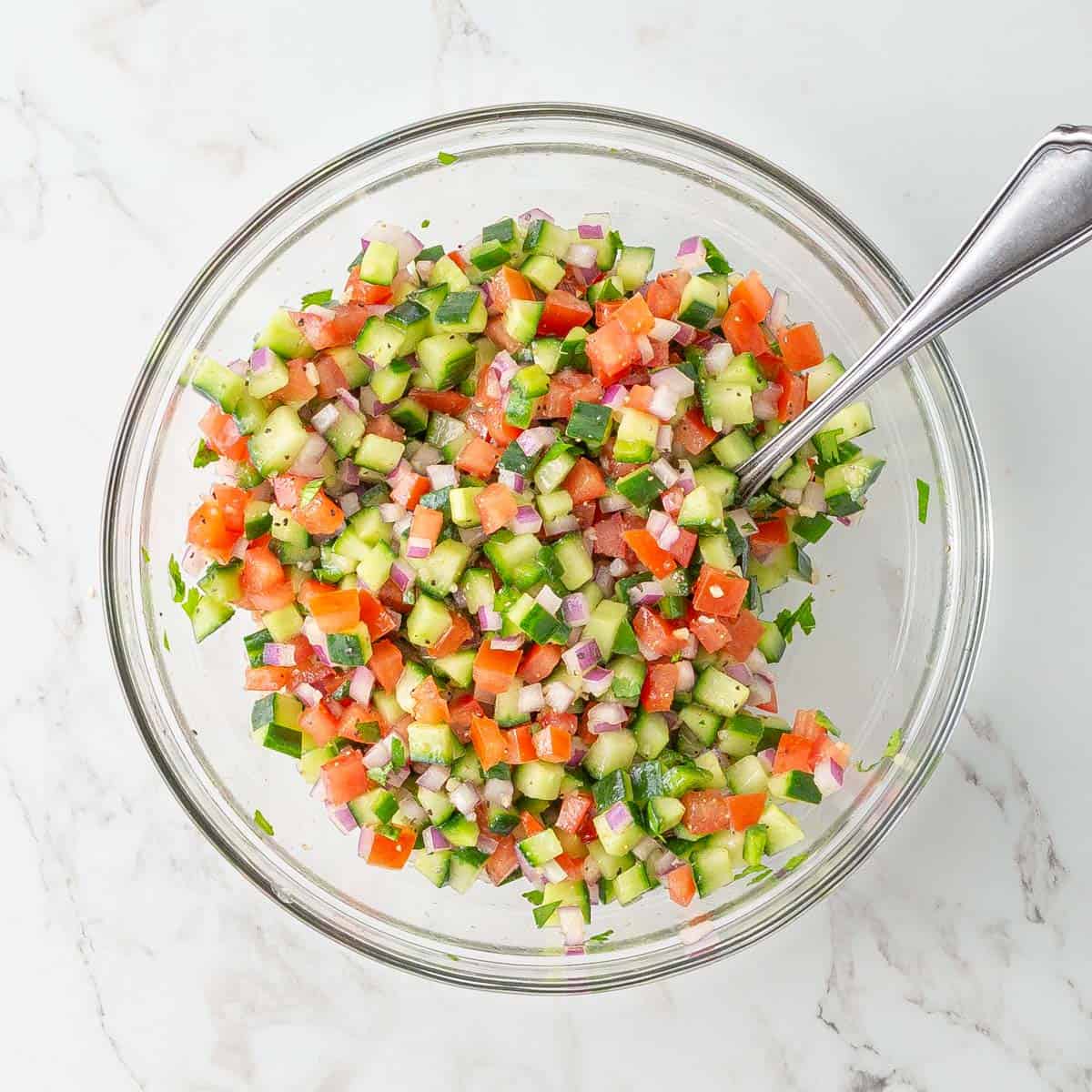 Overhead view of cucumber salsa in a mixing bowl with a large spoon.