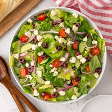 Mediterranean salad in a white bowl beside a pair of wooden salad servers.