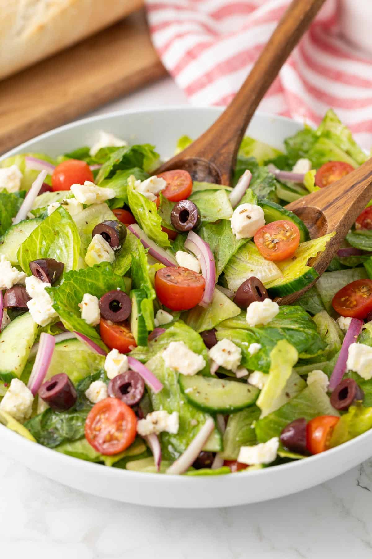 A pair of wooden salad servers in a bowl of Mediterranean Greek salad.