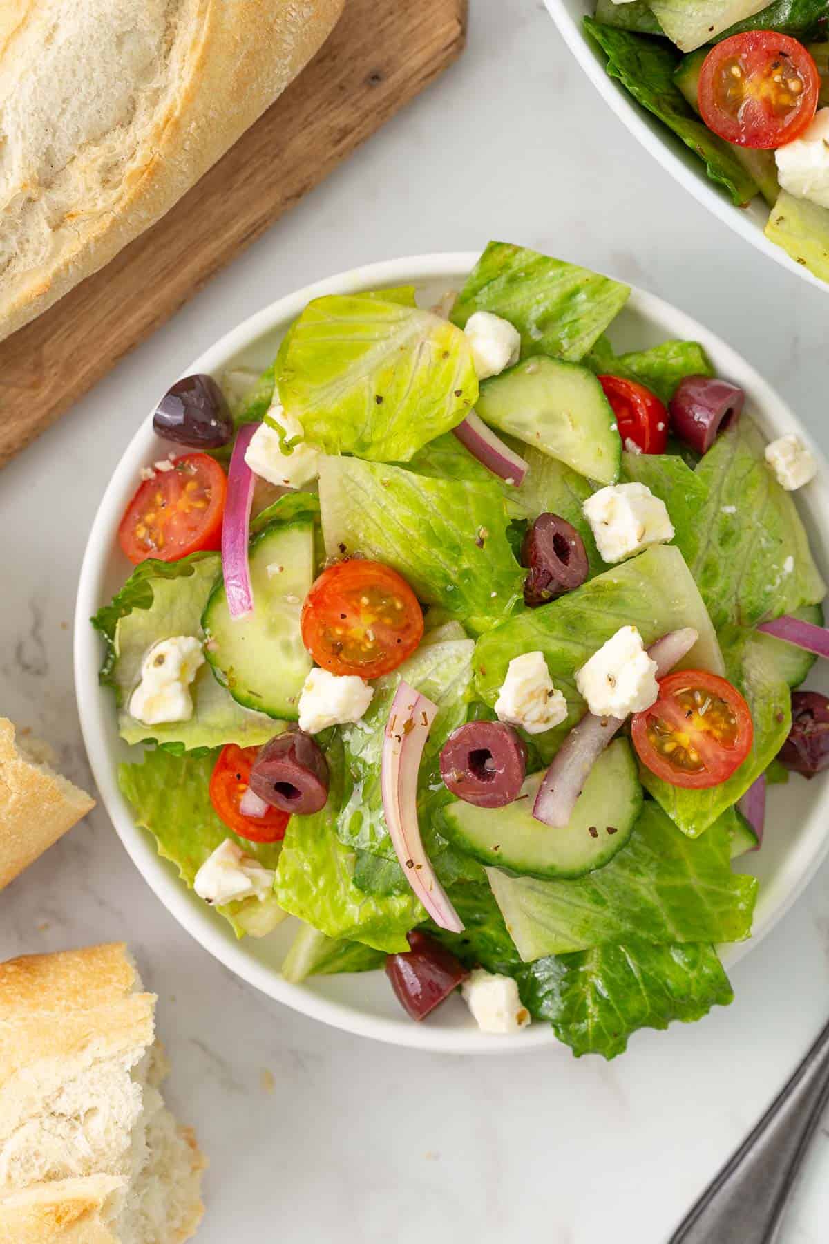 A bowl of Mediterranean salad beside a French baguette.