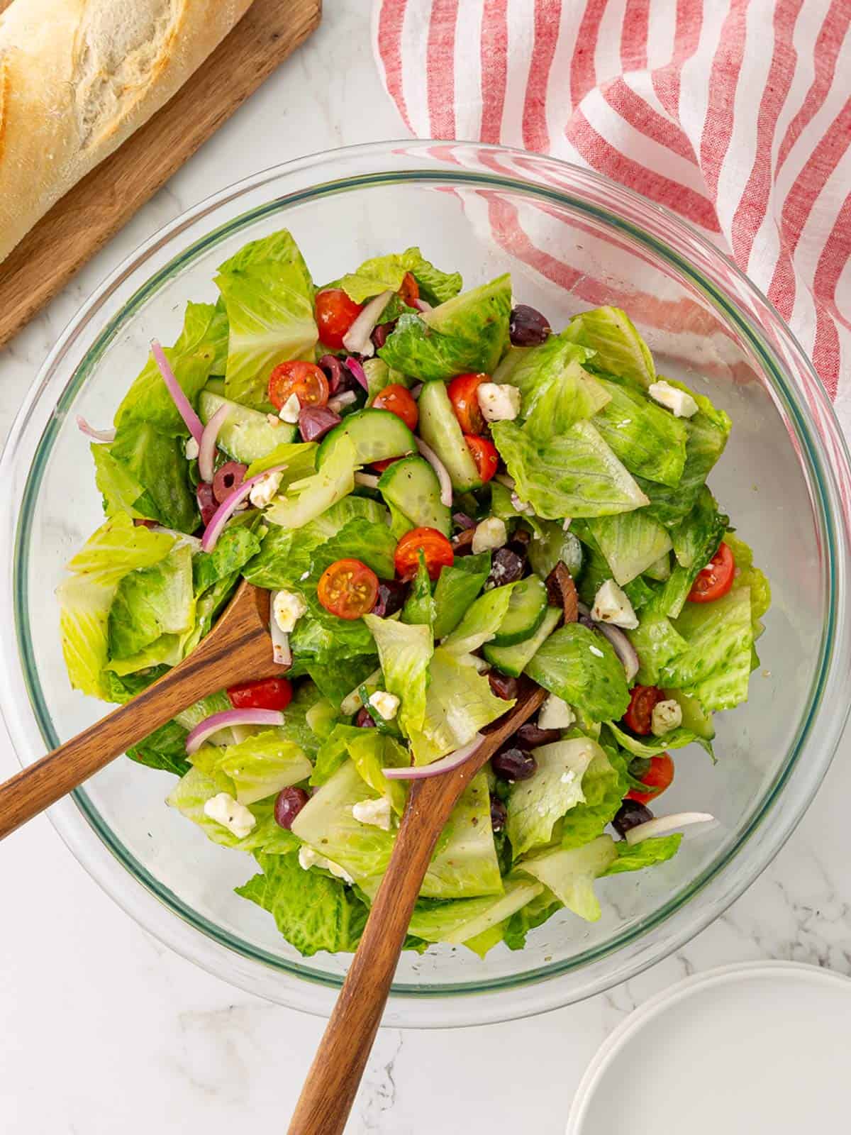 A Mediterranean salad is tossed with dressing in a glass bowl.