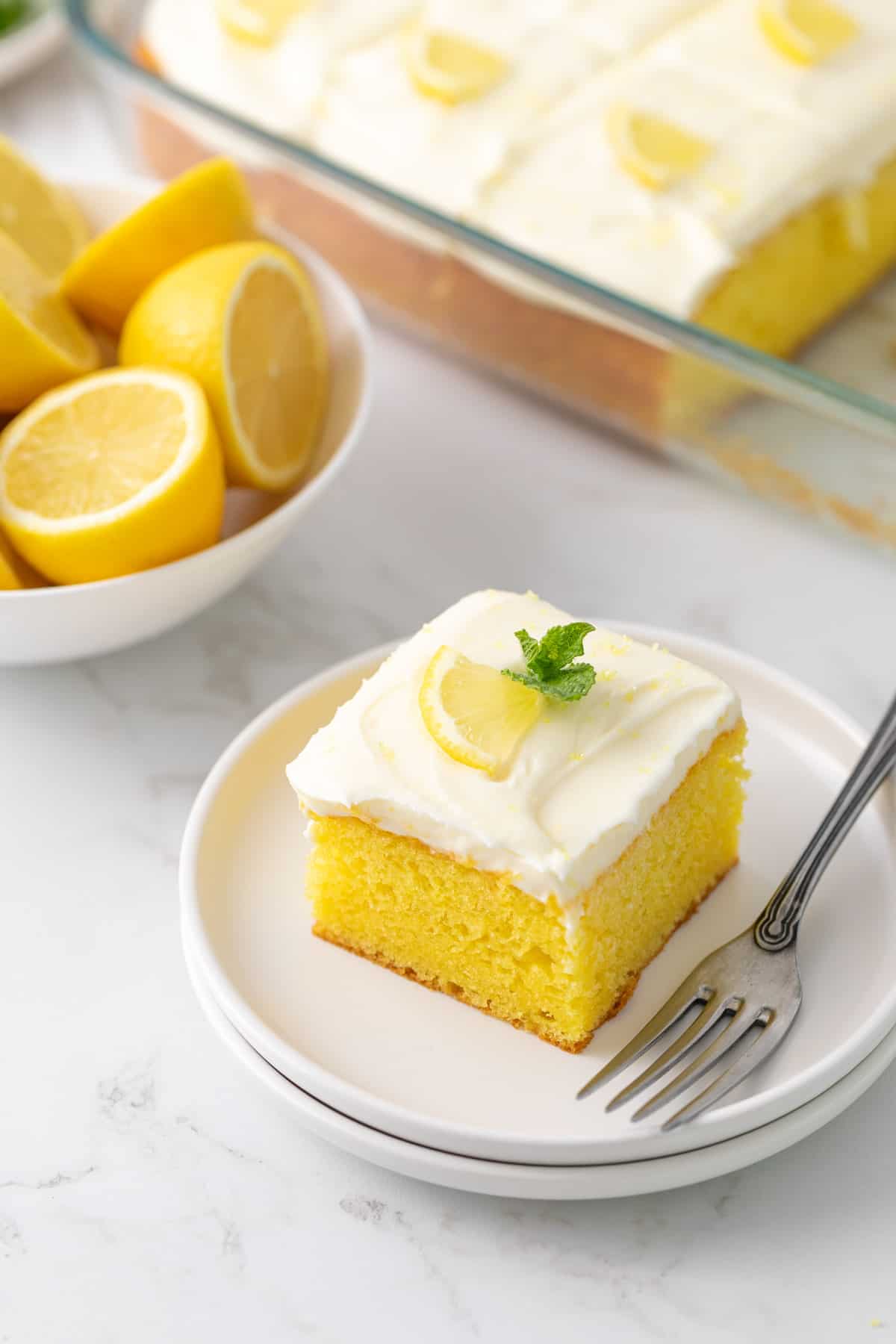A slice of lemon sheet cake frosted with cream cheese frosting on a dessert plate with a fork.