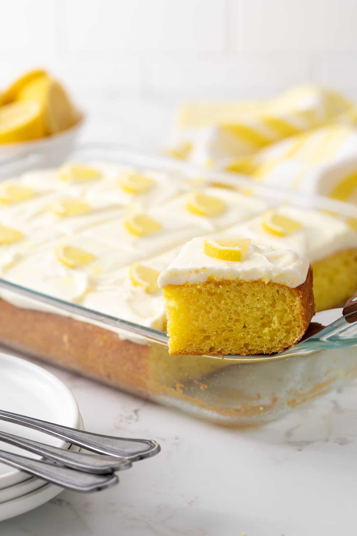 A spatula removing a slice of lemon sheet cake from a glass 13 x 9 baking dish.