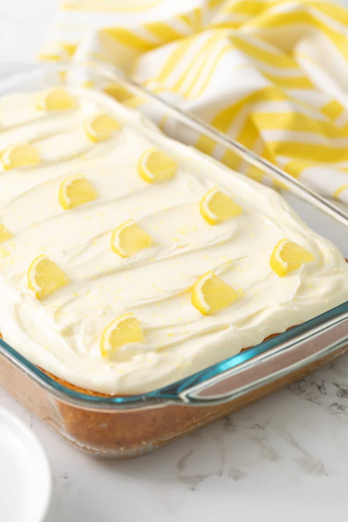 A frosted lemon sheet cake decorated with lemon slices and yellow sugar.