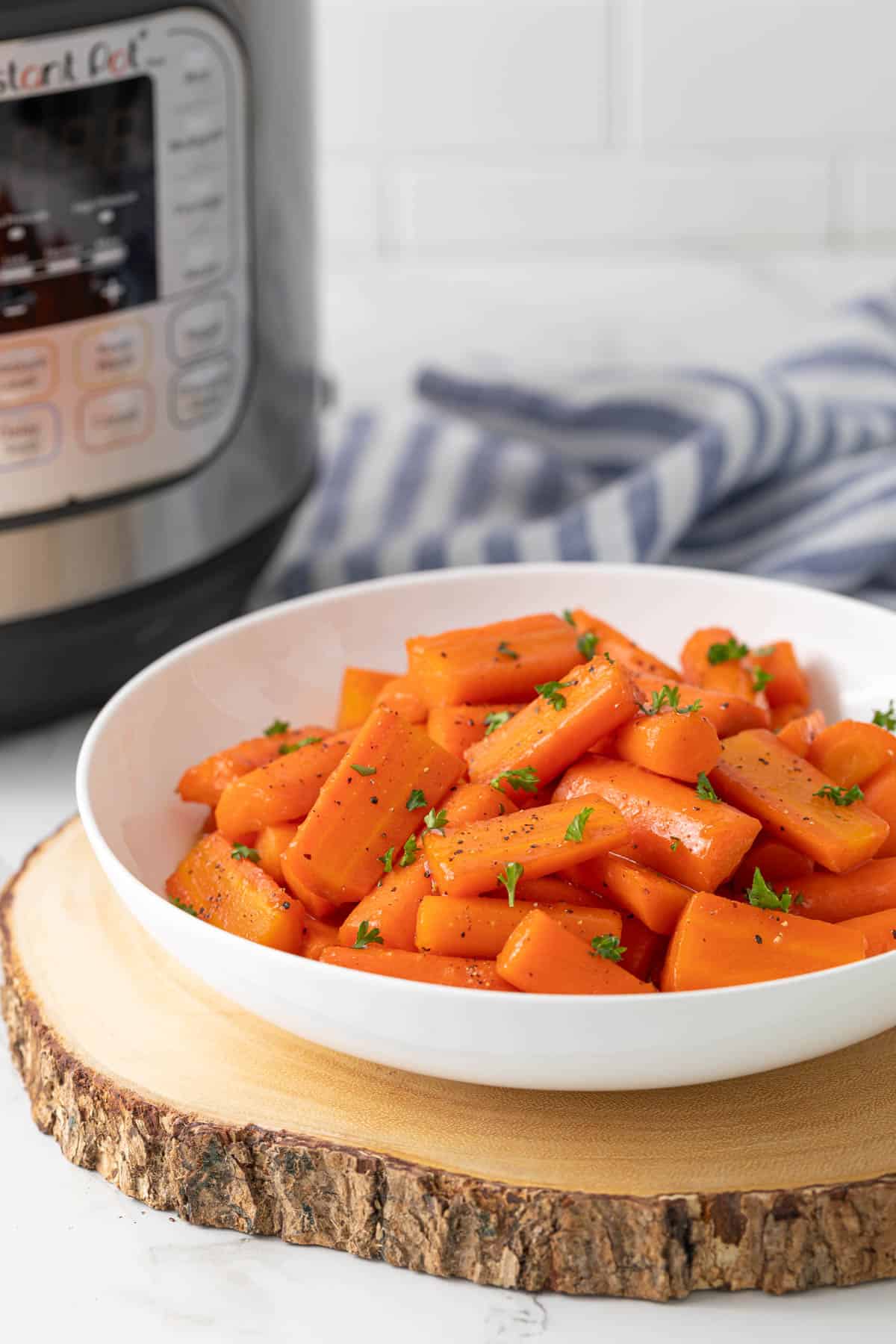 Glazed carrots in a white bowl. An Instant Pot pressure cooker is in the background.