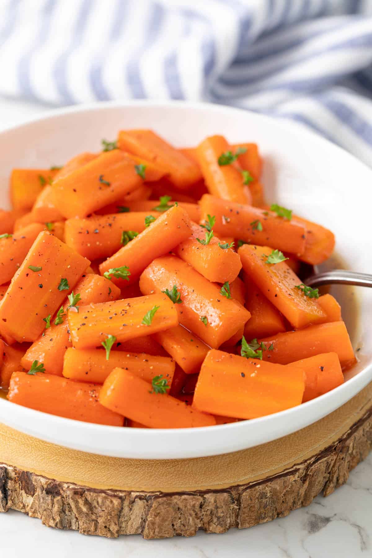 Glazed carrots in a white bowl with a serving spoon.
