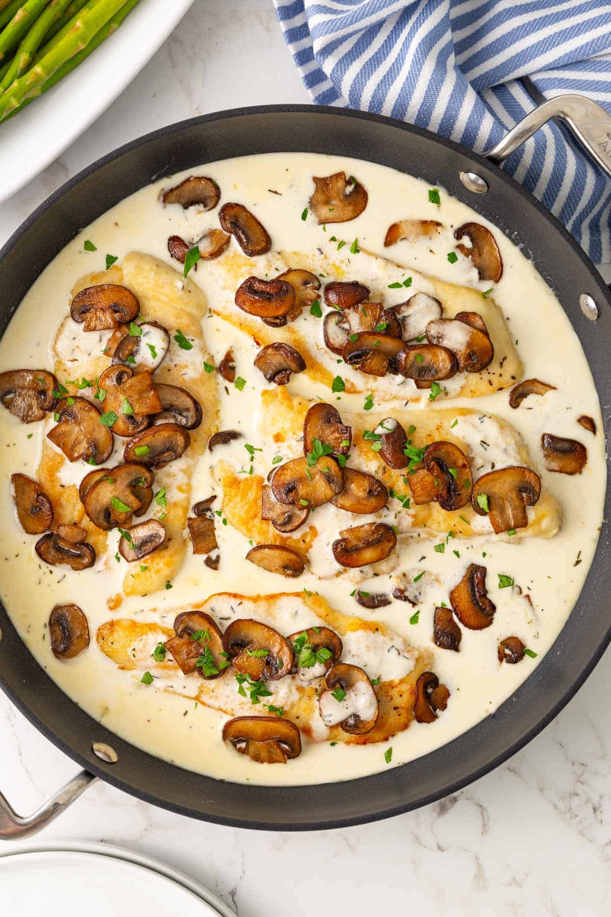 Overhead view of chicken breasts in a skillet with creamy mushroom sauce.