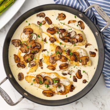 Overhead view of cooked chicken breast cutlets in a skillet with creamy mushroom sauce.