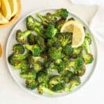 Overhead view of broccoli that has been cooked in an air fryer on a white plate.