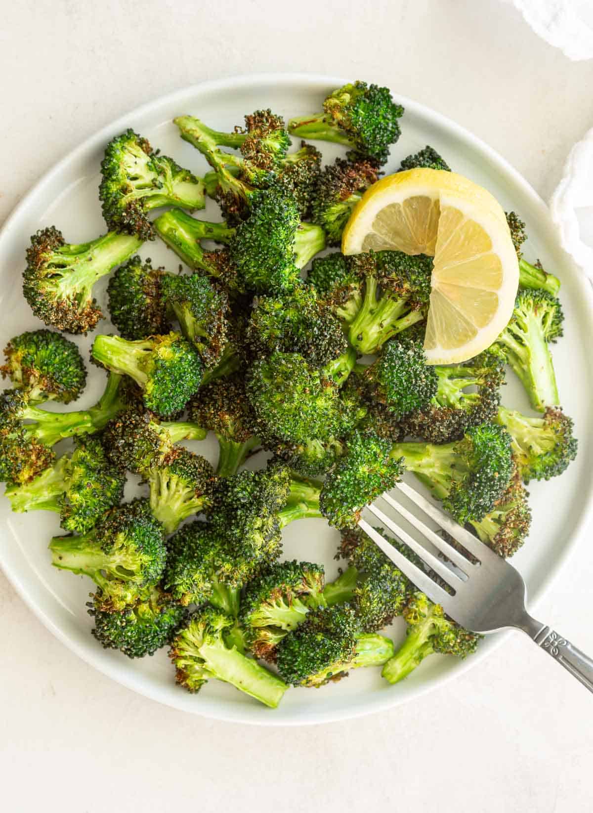 Air-fried broccoli florets on a white plate with a fork.