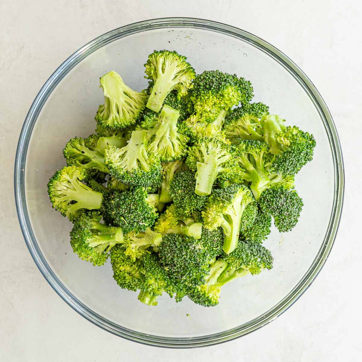 Broccoli florets that have been tossed with olive oil and seasonings in a bowl.
