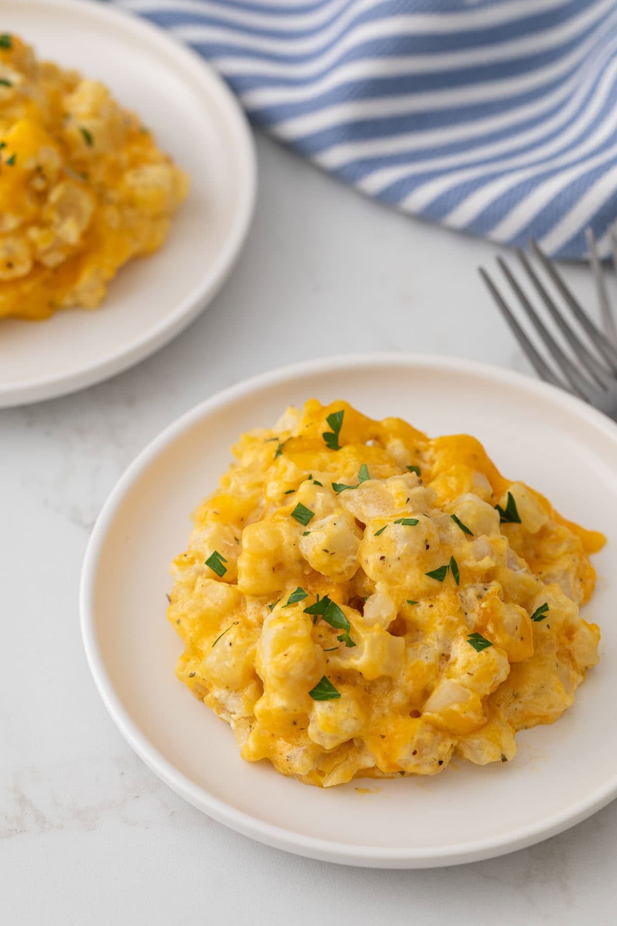 Crockpot cheesy potatoes on two white plates on a marble surface.
