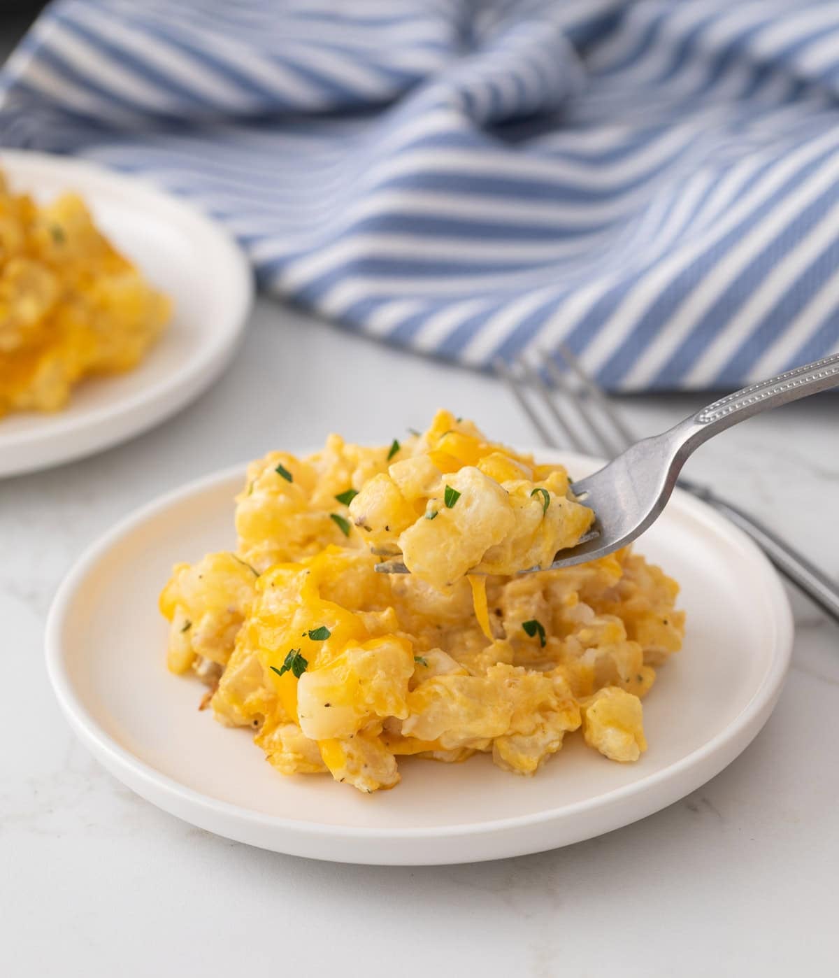 A fork scooping up cheesy potatoes from a small white plate.