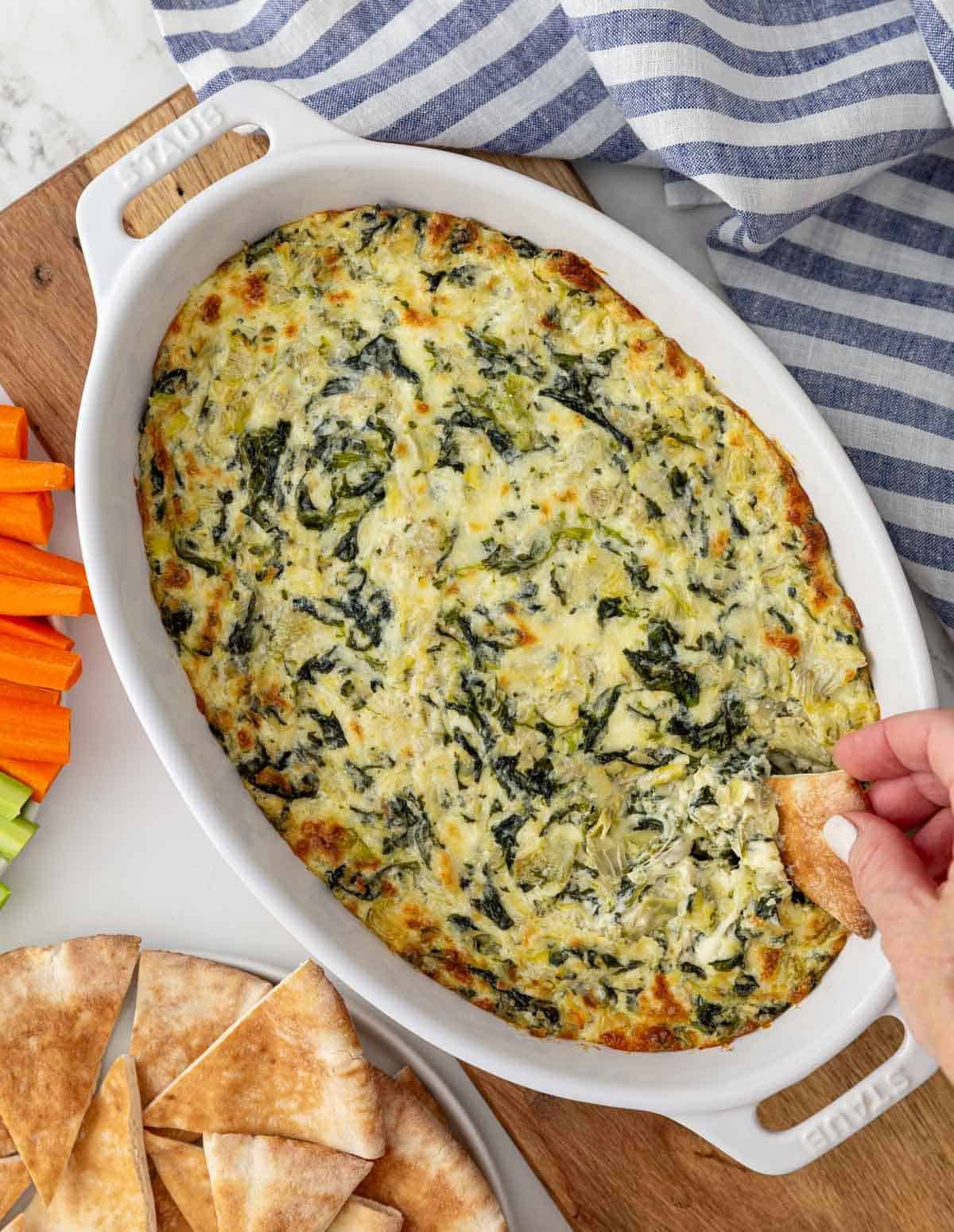 Overhead view of a pita point being dipped into a dish of spinach artichoke dip.