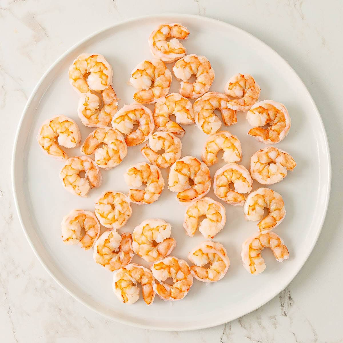Cooked shrimp that have been patted dry on a white plate.