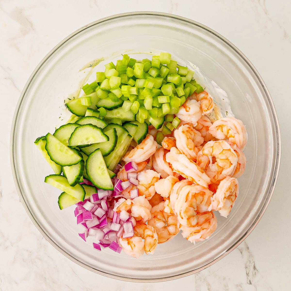 Cucumber and shrimp salad ingredients added in segments on top of dressing in a bowl.