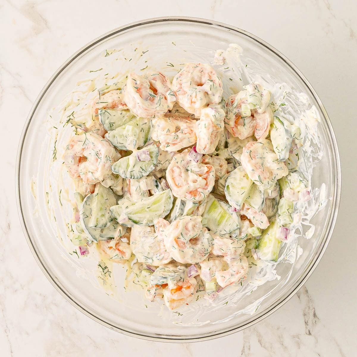 Cucumber and shrimp salad ingredients stirred together in a bowl.