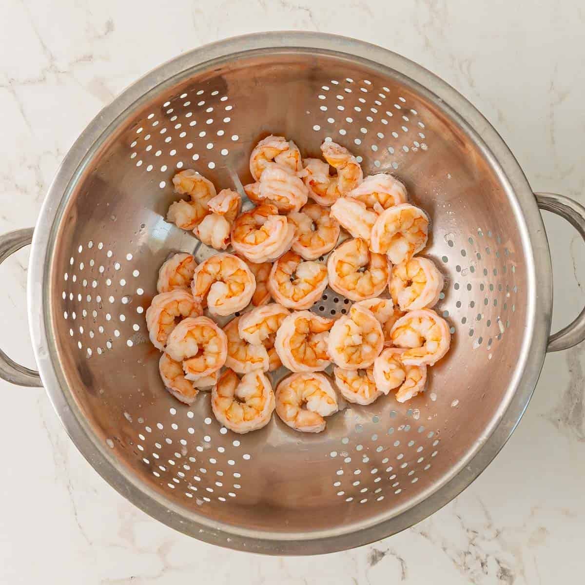 Drained cooked shrimp in a colander.