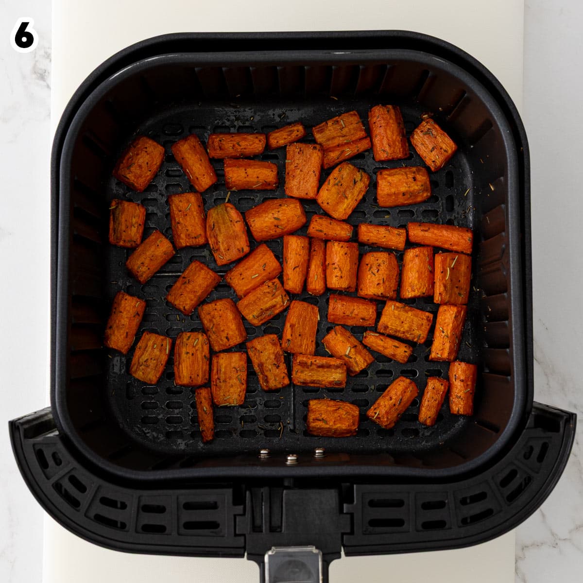 Overhead view of seasoned carrot pieces in an air fryer basket after air frying.