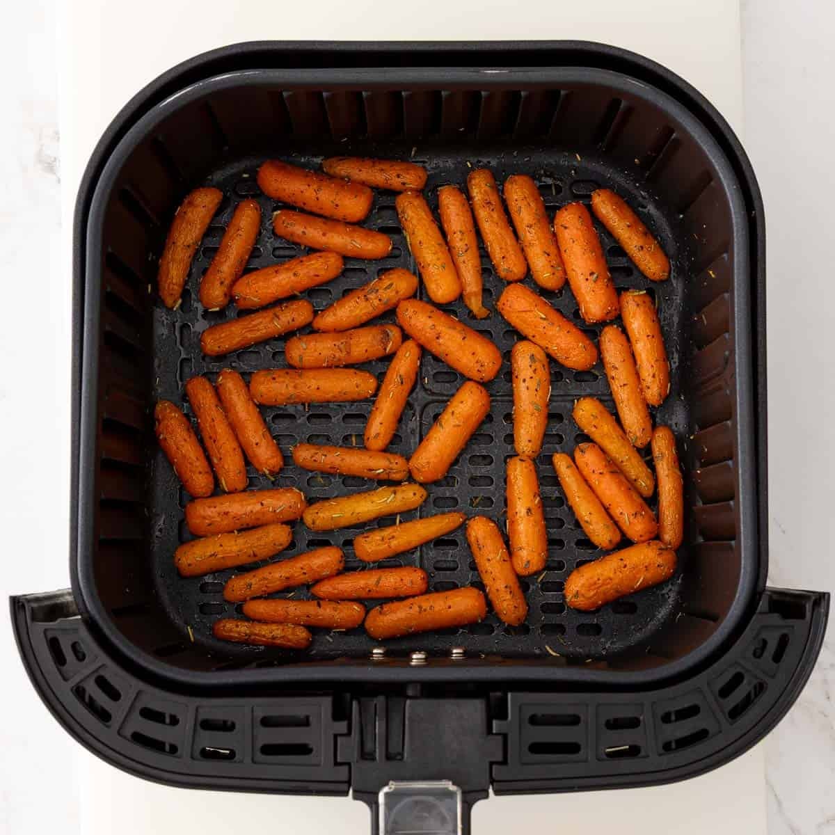 Overhead view of air fried baby carrots in an air fryer basket.