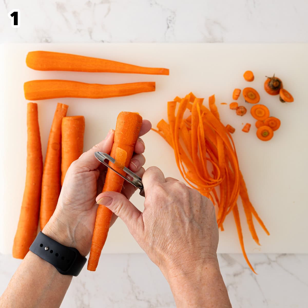 Overhead view of a carrot being peeled over a white cutting board.