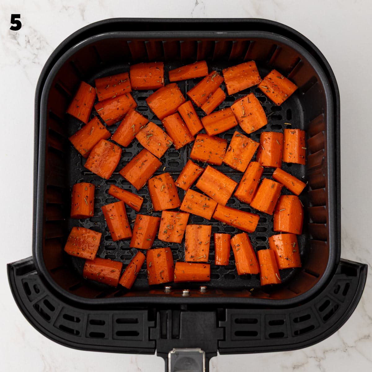 Overhead view of seasoned carrot pieces in an air fryer basket before air frying.