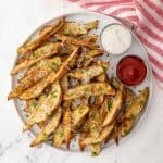 Overhead view of baked potato wedges on a white plate with ranch dressing and ketchup in condiment cups.