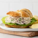 Front view of a chicken salad croissant on a plate with potato chips.