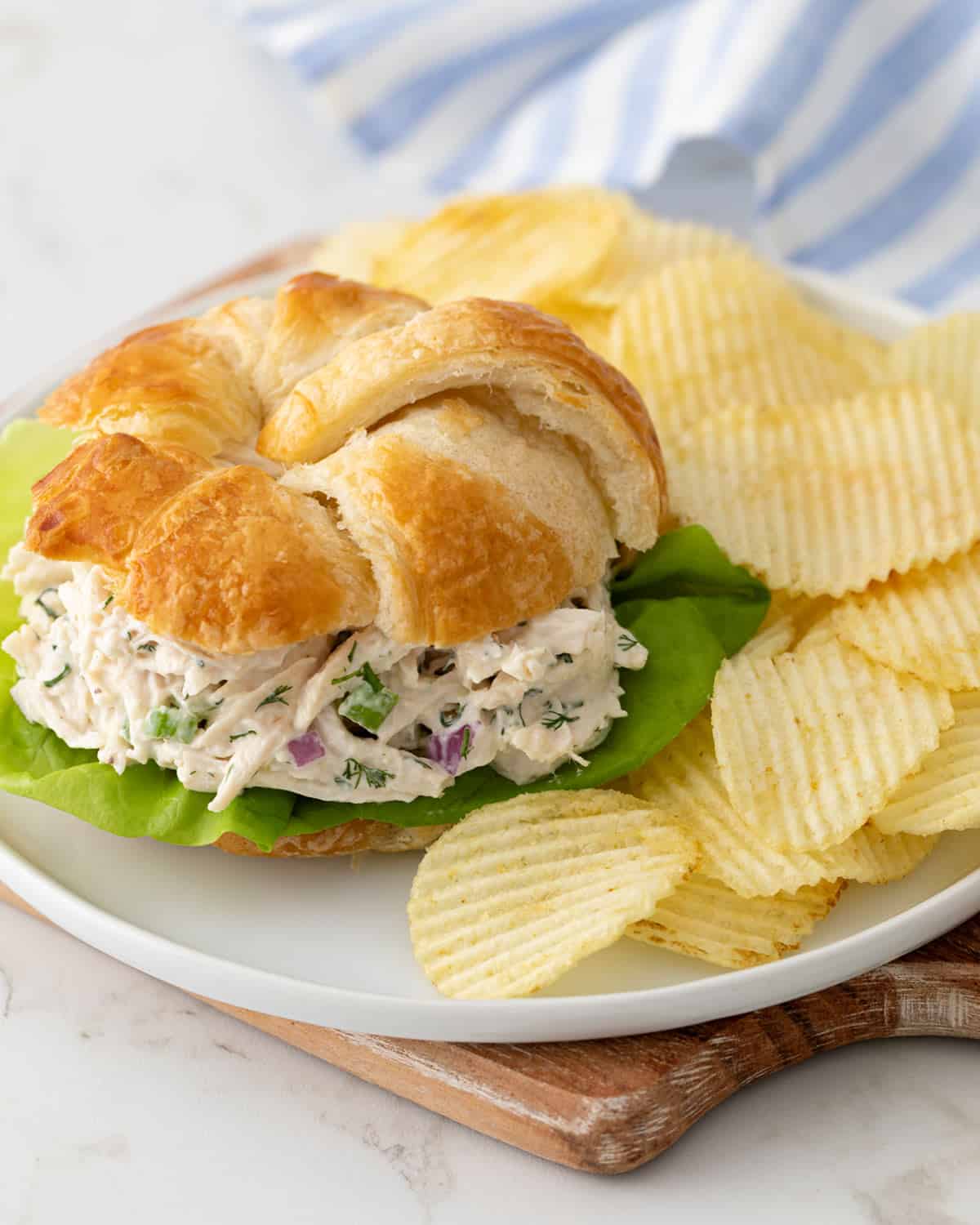 Front angled view of a chicken salad croissant on a white plate with potato chips.