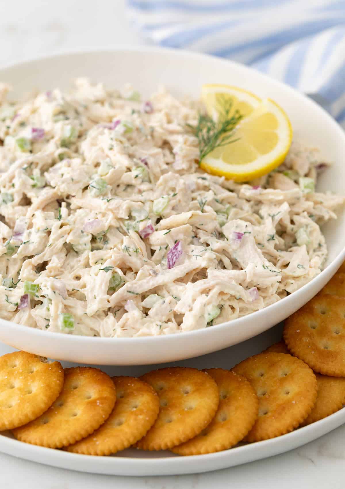 Angled view of a bowl of classic chicken salad on a serving plate with crackers.