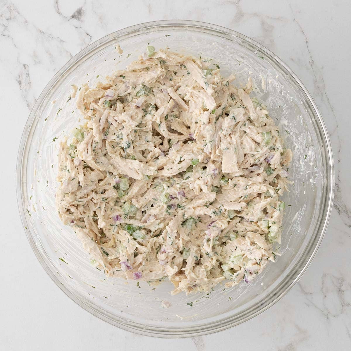 Chicken, celery, and onions have been added to dressing in a bowl and combined to make chicken salad.