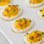 A close up angled view of pimento cheese deviled eggs on a white platter.
