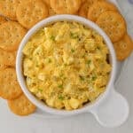 Overhead view of egg salad in a white bowl on a plate with crackers.