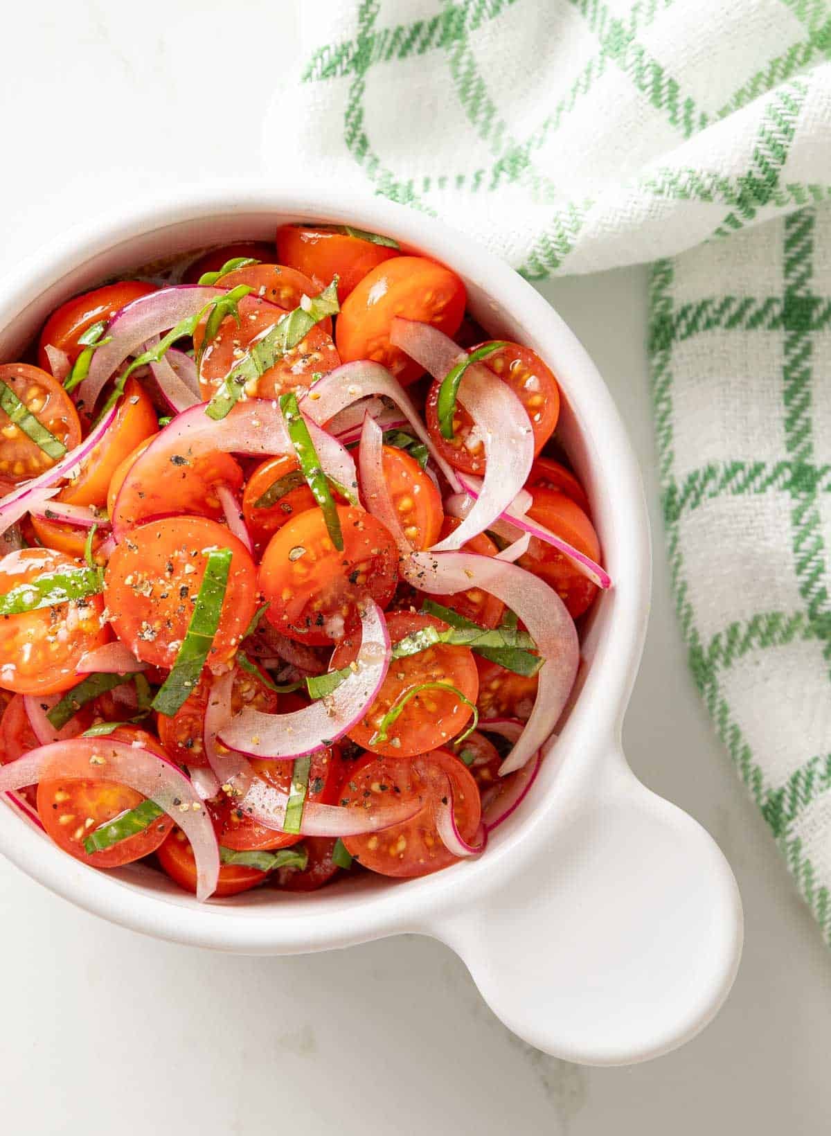 Overhead view of tomato and red onion salad with basil in a white bowl.