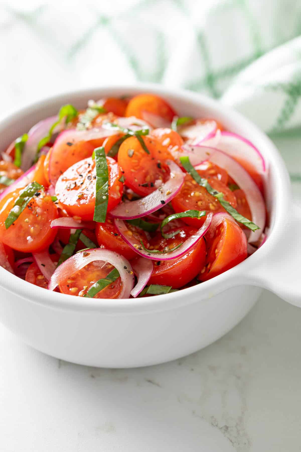 Tomato and red onion salad in a white bowl.