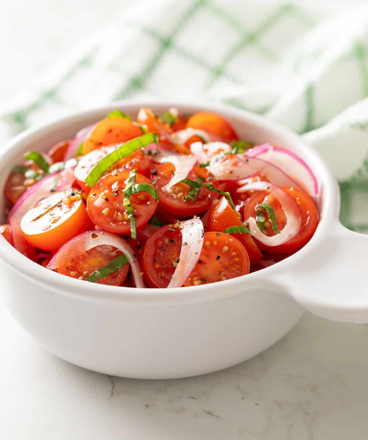 Tomato and red onion salad in a white bowl.